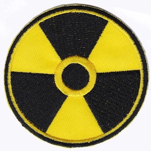 Könnte beinhalten: Ein gelber und schwarzer gestickter Aufnäher mit einem Strahlungssymbol. Das Symbol ist ein stilisiertes dreiblättriges Kleeblatt mit einem schwarzen Kreis in der Mitte.