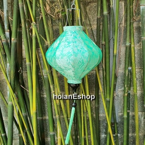 May include: A green silk lantern with a white floral pattern hangs from a bamboo stand. The lantern has a tassel and a black finial.