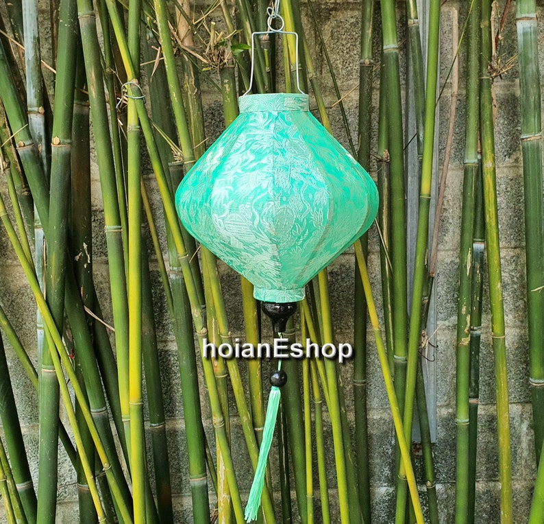 May include: A green silk lantern with a white floral pattern hangs from a bamboo stand. The lantern has a tassel and a black finial.