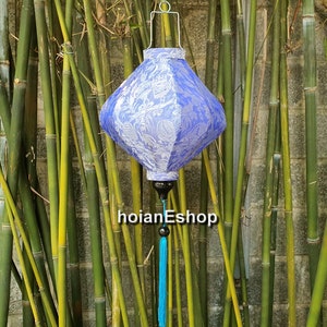May include: A blue and white silk lantern with a tassel hanging from the bottom. The lantern is hanging from a hook in front of a bamboo wall.