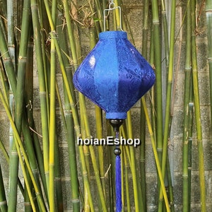 May include: A blue silk lantern with a diamond shape and intricate floral patterns. The lantern is hanging from a bamboo background.