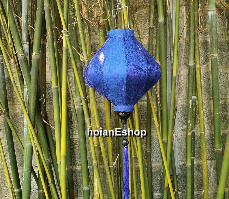 May include: A blue silk lantern with a diamond shape and intricate floral patterns. The lantern is hanging from a bamboo background.