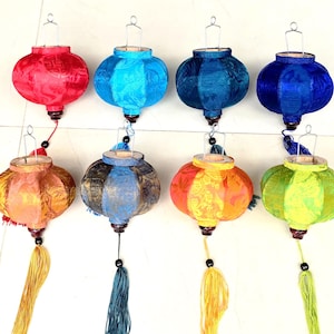 Könnte beinhalten: Acht Seidenlaternen in verschiedenen Farben, darunter Rot, Blau, Grün, Gelb und Orange. Jede Laterne hat einen Quasten, der an der Unterseite hängt.