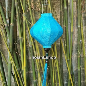 May include: A blue silk lantern with a tassel hanging from the bottom. The lantern has a white design and is hanging from a bamboo background.