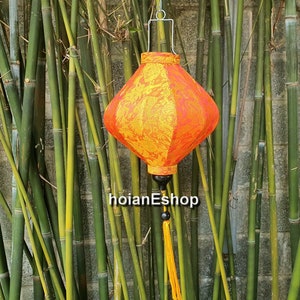May include: A red and yellow silk lantern with a gold tassel hanging from a bamboo background.