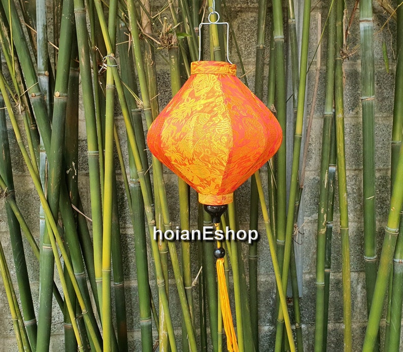 May include: A red and yellow silk lantern with a gold tassel hanging from a bamboo background.