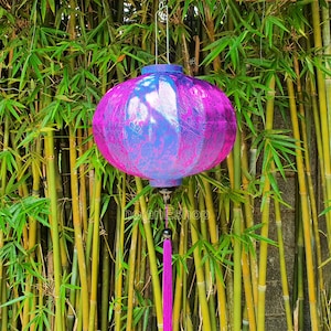 May include: A purple and blue silk lantern with a tassel hanging from the bottom. The lantern is hanging from a bamboo background.