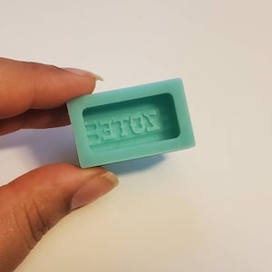 Op de afbeelding: Een lichtblauwe siliconen mal voor het maken van zeep of hars. De mal heeft het woord "BEAST" in reliëf in het midden.