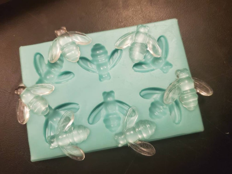 May include: A silicone mold with eight bee-shaped cavities. The mold is light blue and the bees are clear.
