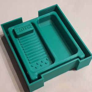 May include: A green plastic tray with two compartments. The larger compartment has a raised section with the word "ZOTTER" printed on it. The smaller compartment is smooth.