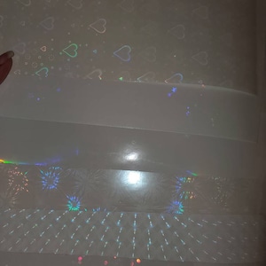 May include: A sheet of iridescent holographic paper with a variety of patterns. The patterns include hearts, fireworks, and a grid.