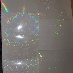 May include: A set of eight iridescent holographic sheets with different patterns. The patterns include stars, hearts, fireworks, and geometric shapes.