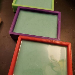 May include: Three rectangular soap molds, one red, one purple, and one green, with a light green soap inside each.