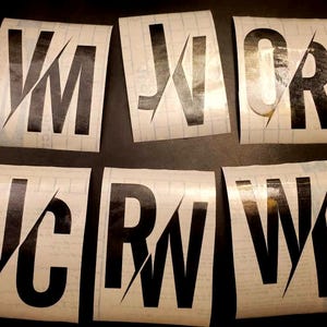 Könnte beinhalten: Sechs weiße rechteckige Aufkleber mit schwarzen Buchstaben. Jeder Aufkleber hat zwei Buchstaben, die halbiert und überlappt sind. Die Buchstaben sind: JM, OR, WF, RW, JC und VW.