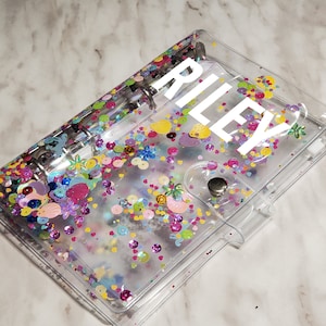 Könnte beinhalten: Ein transparenter Plastikordner mit einem bunten Konfetti-Design und dem Namen "RILEY" auf der Vorderseite.