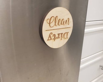 Könnte beinhalten: Ein rundes Schild aus Holz mit den Worten "Dreckig" und "Sauber" darauf. Das Schild ist an einem Edelstahl-Geschirrspüler befestigt.