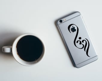 以下が含まれることがあります： 背面に黒いステッカーが貼られたシルバーのiPhone。ステッカーは、アップルのロゴが組み込まれた「Om」という単語のスタイリッシュなデザインです。白いコーヒーカップに黒いコーヒーが入っており、白い表面の上に置かれています。