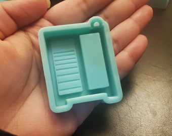 May include: A light blue silicone mold shaped like a small refrigerator with a rectangular opening and a smaller rectangular opening with lines inside.