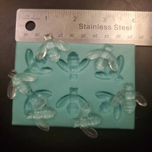 May include: A silicone mold with eight cavities shaped like bees. The mold is light blue and has a ruler with the words "Inches Pouces" and "Stainless Steel" printed on it.