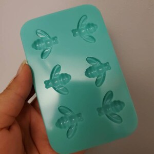 May include: A teal silicone mold with six bee-shaped cavities. The mold is designed for making small, bee-shaped candies, chocolates, or other treats.