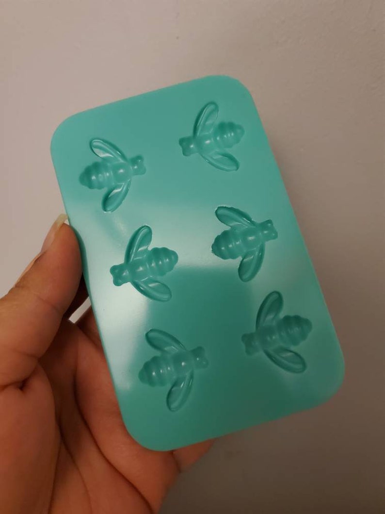 May include: A teal silicone mold with six bee-shaped cavities. The mold is designed for making small, bee-shaped candies, chocolates, or other treats.