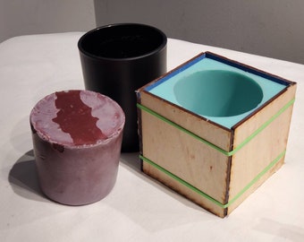 May include: A wooden box with a teal silicone mould inside, secured with rubber bands. A purple candle and a black container are also visible.