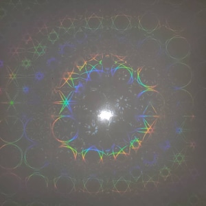 May include: A white sheet of paper with a holographic pattern of circles, stars, and geometric shapes in rainbow colors.