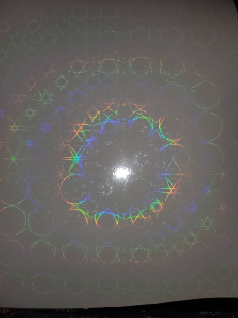 May include: A white sheet of paper with a holographic pattern of circles, stars, and geometric shapes in rainbow colors.