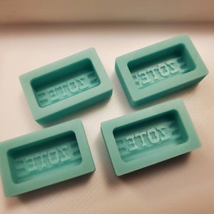 May include: Four teal blue silicone molds with the word "VOTE" embossed in each mold.