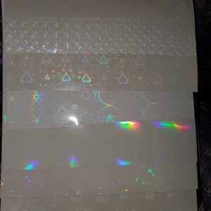 May include: A set of six iridescent holographic sheets with different patterns. The patterns include hearts, stars, and fireworks.