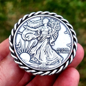 Może przedstawiać: Srebrna amerykańska półdolarowa moneta Walking Liberty z ozdobnym, sznurowym rantem. Na monecie widnieje wizerunek Liberty idącej, trzymającej gałązkę laurową i gałązkę oliwną. Na monecie wygrawerowano rok 2000. Na monecie wygrawerowano napis "In God We Trust".