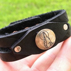 May include: Black leather bracelet with a silver-toned wolf howling at the moon charm.