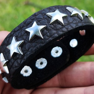 May include: Black leather bracelet with silver star studs and silver metal accents.