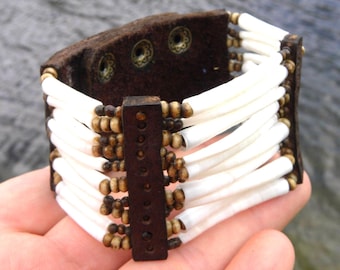 May include: A brown leather bracelet with white and brown beads. The bracelet has a buckle closure and is decorated with metal studs.