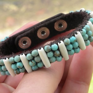 May include: A turquoise and white beaded bracelet with a brown leather strap and adjustable snap closure.