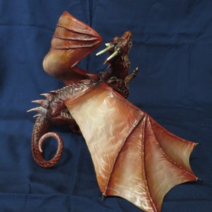 May include: A detailed, red and brown dragon figurine with outstretched wings. The dragon has a textured body, sharp claws, and a curled tail. The wings are a lighter shade of brown with detailed veining. The dragon is posed with its mouth open, as if roaring.