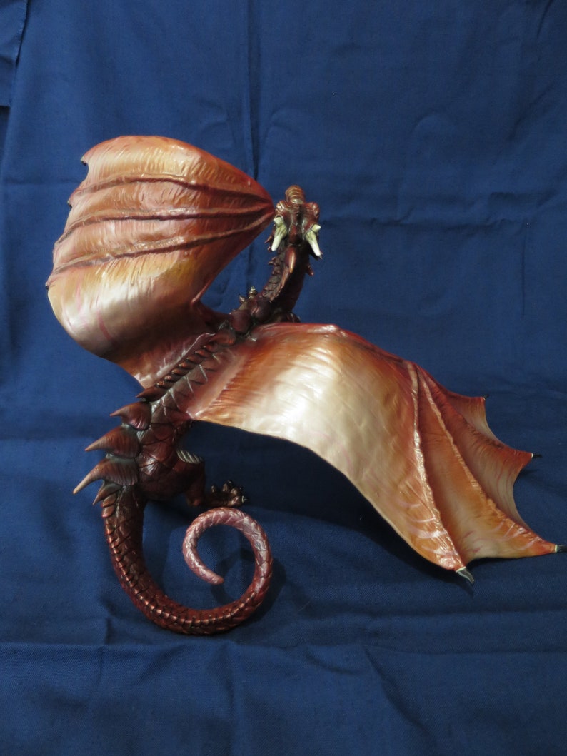 May include: A detailed sculpture of a dragon with outstretched wings and a curled tail. The dragon is primarily brown with lighter shades on the wings, and it appears to be breathing fire. The sculpture is set against a blue background.