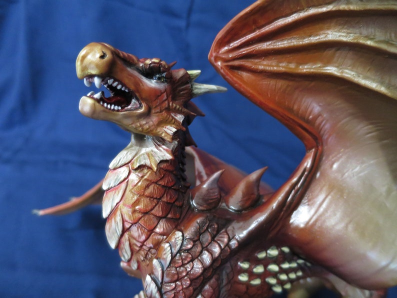 May include: A detailed, red and brown dragon figurine with open mouth, sharp teeth, and detailed scales. The dragon has large wings and is set against a blue background. The figurine is a fantasy-themed collectible.