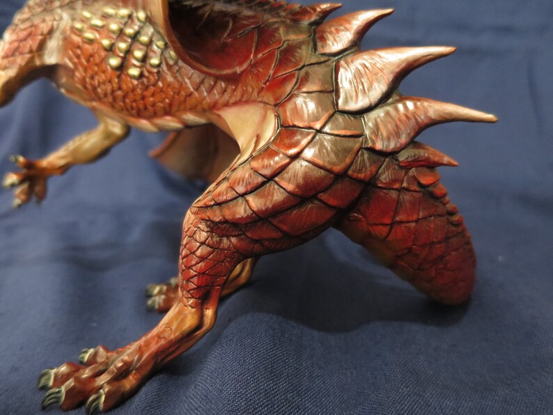 May include: A detailed sculpture of a red and brown dragon with textured scales and sharp spines. The dragon is in a dynamic pose, with its claws extended and wings partially visible. The sculpture has a detailed, realistic appearance.