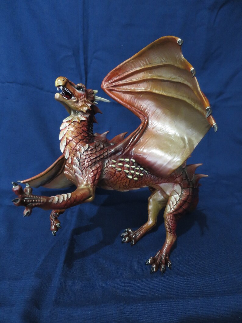 May include: A detailed figurine of a dragon with outstretched wings. The dragon is primarily reddish-brown with lighter accents on the wings and underbelly. Its mouth is open, revealing teeth, and it has sharp claws.