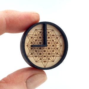May include: A circular plug made of black and wood with a geometric pattern engraved on the wood surface.