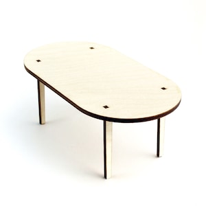 May include: A miniature wooden table with an oval top and four square-shaped insets. The table has four rectangular legs. The wood has a light, natural colour. The table is designed for crafts or dollhouses.