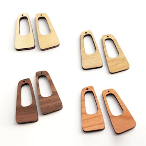May include: Four pairs of wooden earring blanks in various wood tones. Each earring blank has a unique shape with a large cutout and a small hole at the top for attaching to earring hooks. The wood tones include light, medium, and dark browns.