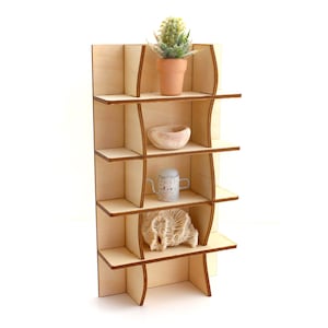 Pode incluir: Uma estante de madeira com cinco prateleiras, cada uma com um objeto decorativo diferente. A prateleira superior tem uma pequena planta suculenta em vaso, a segunda prateleira tem uma pequena tigela branca, a terceira prateleira tem um pequeno regador branco, a quarta prateleira tem um pedaço de coral e a prateleira inferior está vazia.