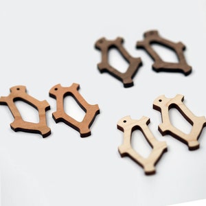 Puede incluir: Varias formas decorativas de madera en tonos marrones. Las formas tienen un diseño geométrico abierto con un pequeño agujero en la parte superior. Los tonos de madera varían de claros a oscuros, creando contraste.