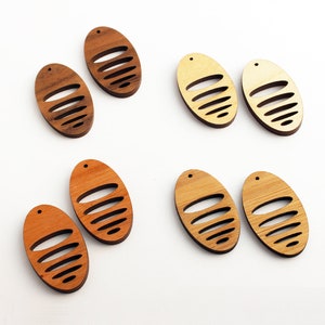 May include: A collection of wooden oval-shaped earrings in various shades of brown and tan. Each earring features a series of horizontal cut-out lines. The earrings have a small hole at the top for hanging. The earrings are displayed on a white surface.