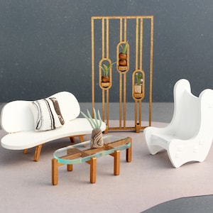 May include: A white, modern sofa with a white and black patterned pillow, a white chair, a gold metal room divider with potted plants, and a glass coffee table with a gold metal frame.