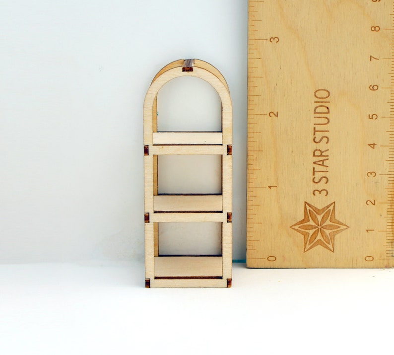 May include: A wooden three-tiered shelf unit with an arched top. The shelf is made of unfinished wood and is approximately 15 cm tall.