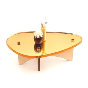 May include: A miniature mid-century modern coffee table with a gold mirrored top and wooden legs. The table is adorned with a small vase and a decorative flower arrangement. The table is approximately 12 inches long.