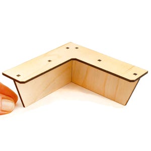 May include: A wooden corner shelf, constructed from light-colored plywood. The shelf is L-shaped with a dark brown edge and small square holes on the top surface. The design is simple and modern, suitable for various home decor styles.